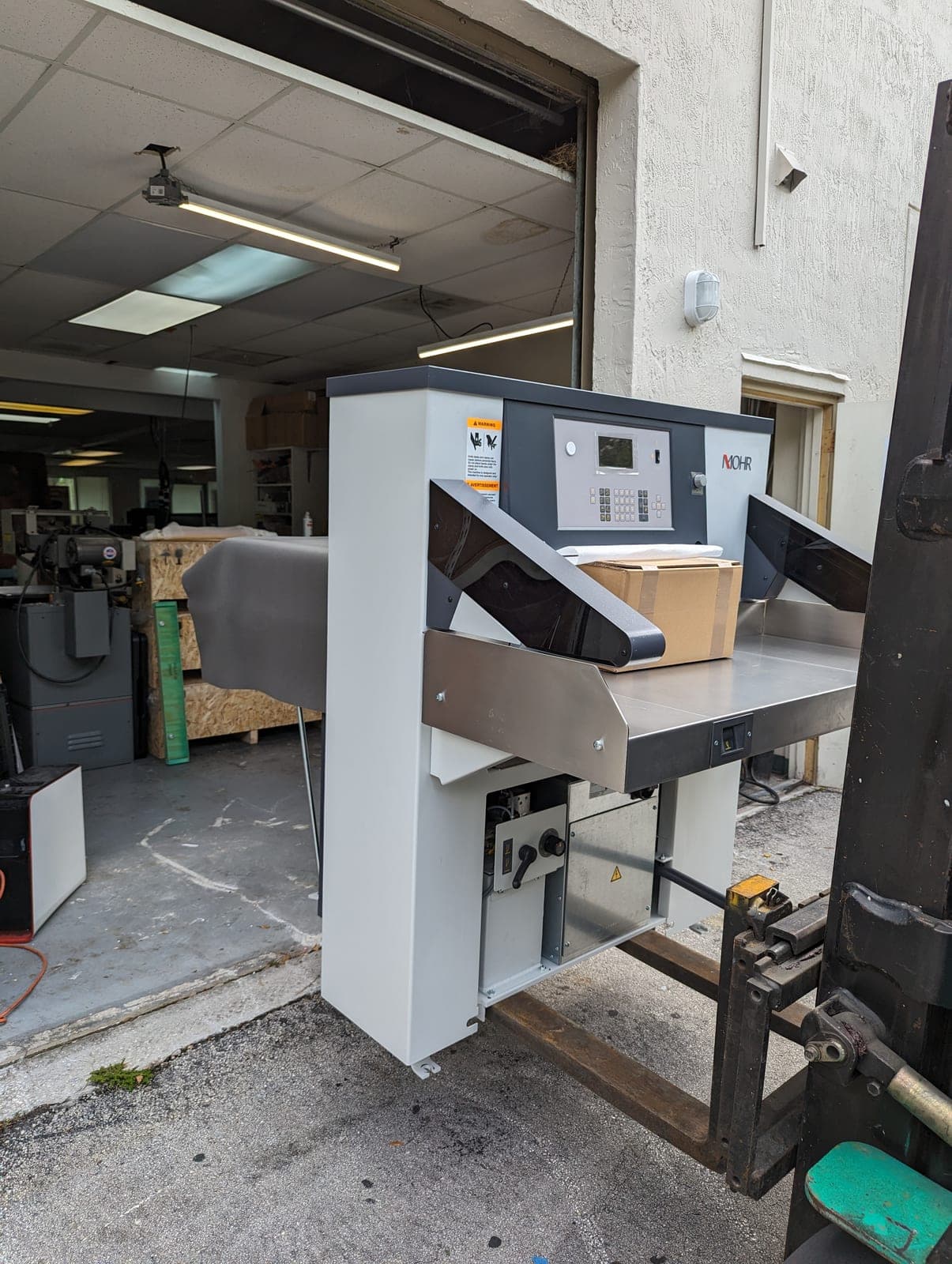 A Mohr paper cutter being moved by forklift into a print shop